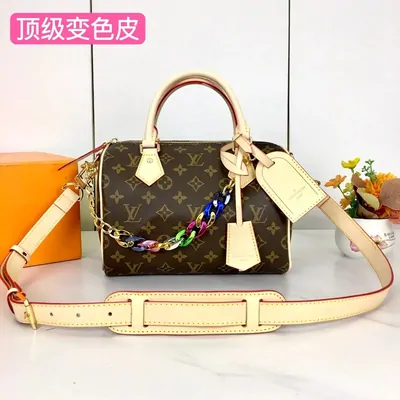 A monogrammed barrel handbag with a multicoloured chain strap and a pale leather shoulder strap, staged beside an orange box.