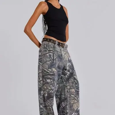 A model from the shoulders down in a black vest top and wide-leg jeans printed with a grey abstract camouflage pattern.