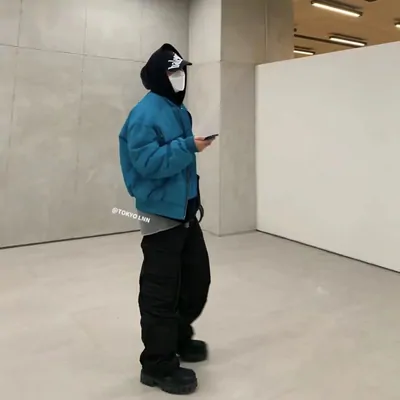 A person indoors in a teal quilted jacket with the hood up, black cargo trousers and black boots, photographed by the seller.