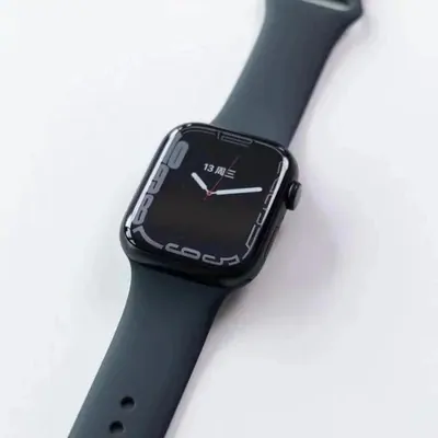 A black rectangular smartwatch with a black silicone strap, photographed diagonally on a pale background.