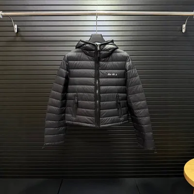 A black quilted hooded down jacket on a hanger in front of a rolled down shop shutter.